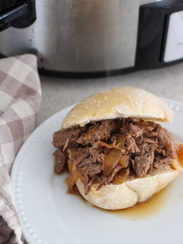 Shredded roast beef on a bun on a white plate with a plaid napkin 