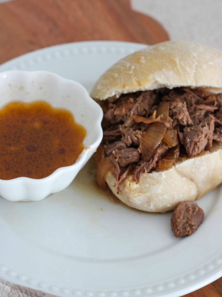 crockpot roast beef on a bun with a side of the juices served on a white plate.