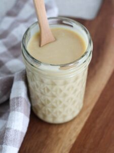 homemade honey mustard in a mason jar on a cutting board with a plaid napkin and wooden spoon