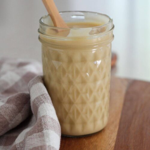 Easy homemade honey mustard dressing in a mason jar with a wooden spoon on a cutting board with a plaid napkin
