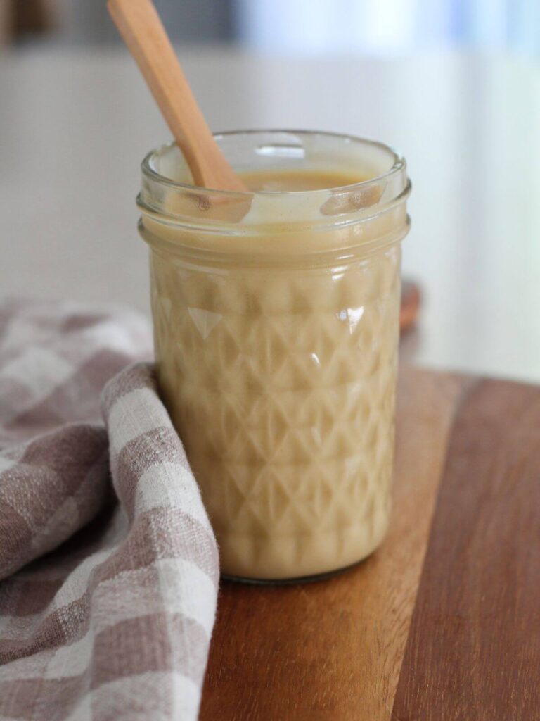 Easy homemade honey mustard dressing in a mason jar with a wooden spoon on a cutting board with a plaid napkin