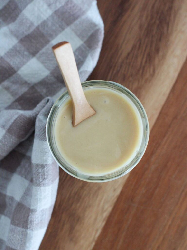 overhead view of the honey mustard in a mason jar with a wooden spoon on a cutting board with a plaid napkin