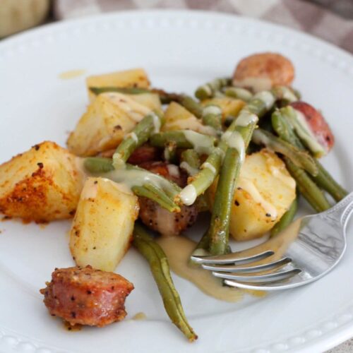 sheet pan chicken sausage dinner plated on a white plate with a silver spoon