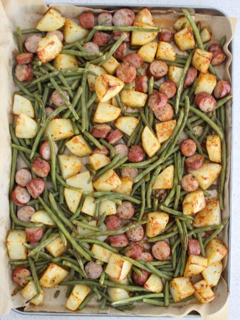 roasted potatoes, chicken sausage and green beans on a sheet pan with parchment paper