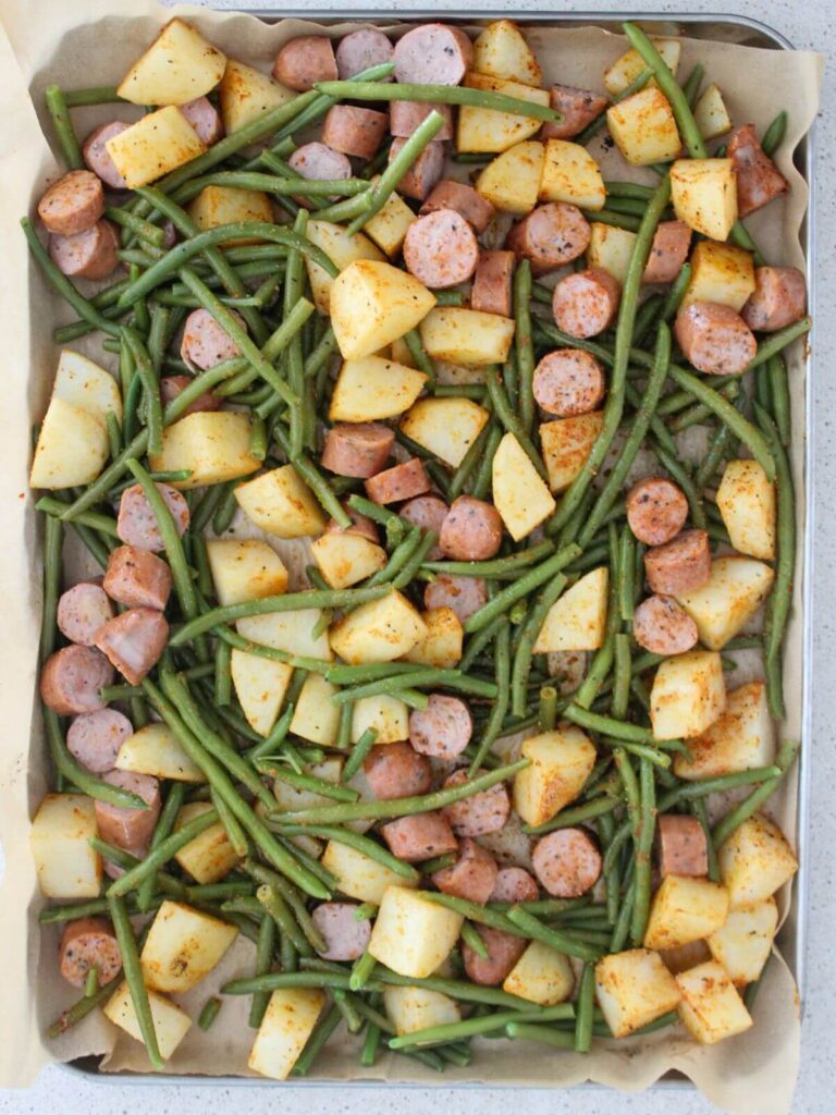 green beans and chicken sausage added to the sheet pan with parchment paper