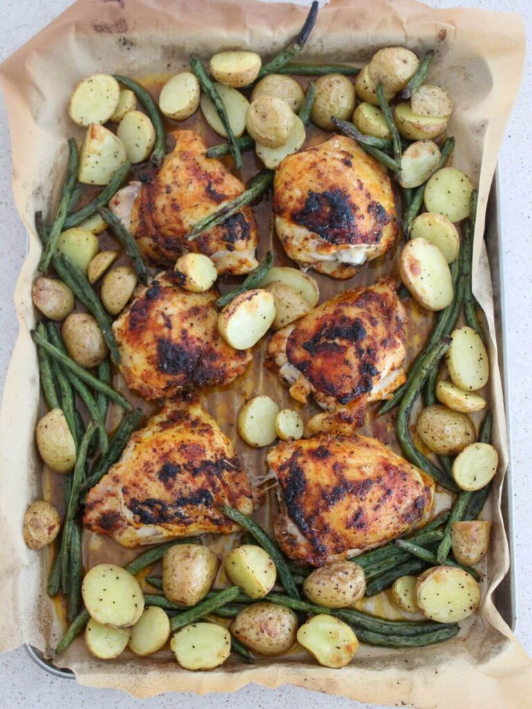 chicken, green beans and potato baked and roasted on a sheet pan lined with parchment paper