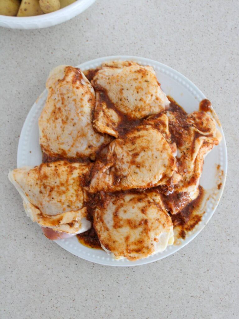 Chicken thighs on a white plate covered in the lemon marinade