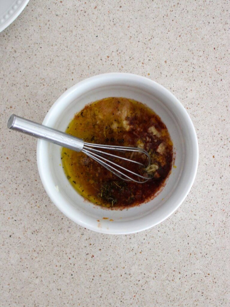 all of the ingredients for the lemon marinade in a white bowl with a stainless steel whisk