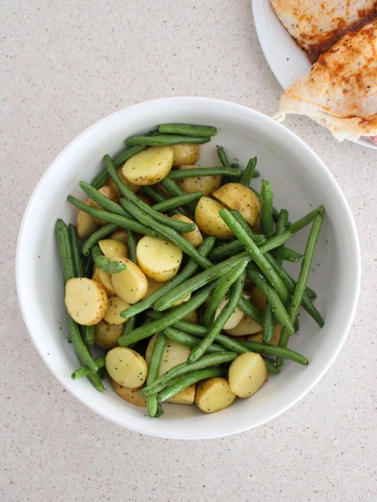 green beans and potatoes in a white bowl with olive oil and Salt and pepper mixed in 