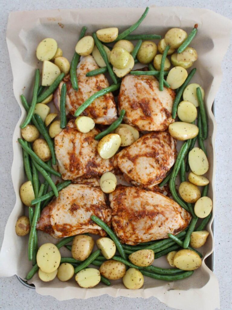chicken thighs, green beans and potatoes arranged on a sheet pan lined with parchment paper