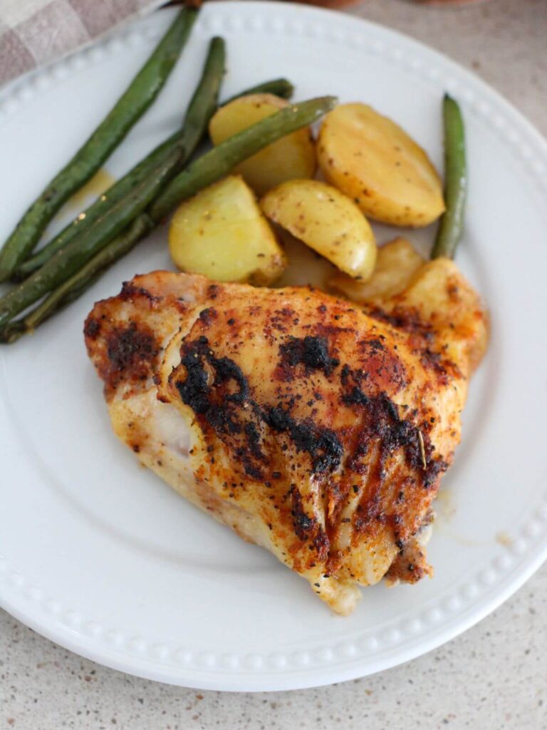 a chicken thigh, some green beans and potatoes on a white plate ready to eat