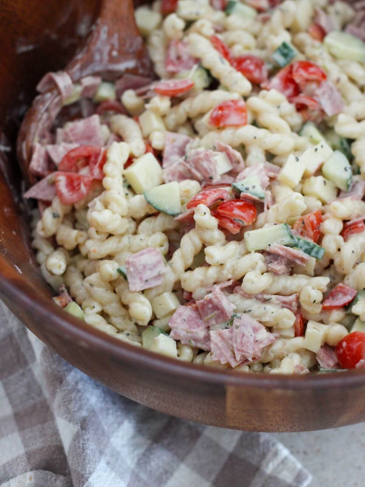 up close of the pasta salad in the wooden bowl with a wooden spoon