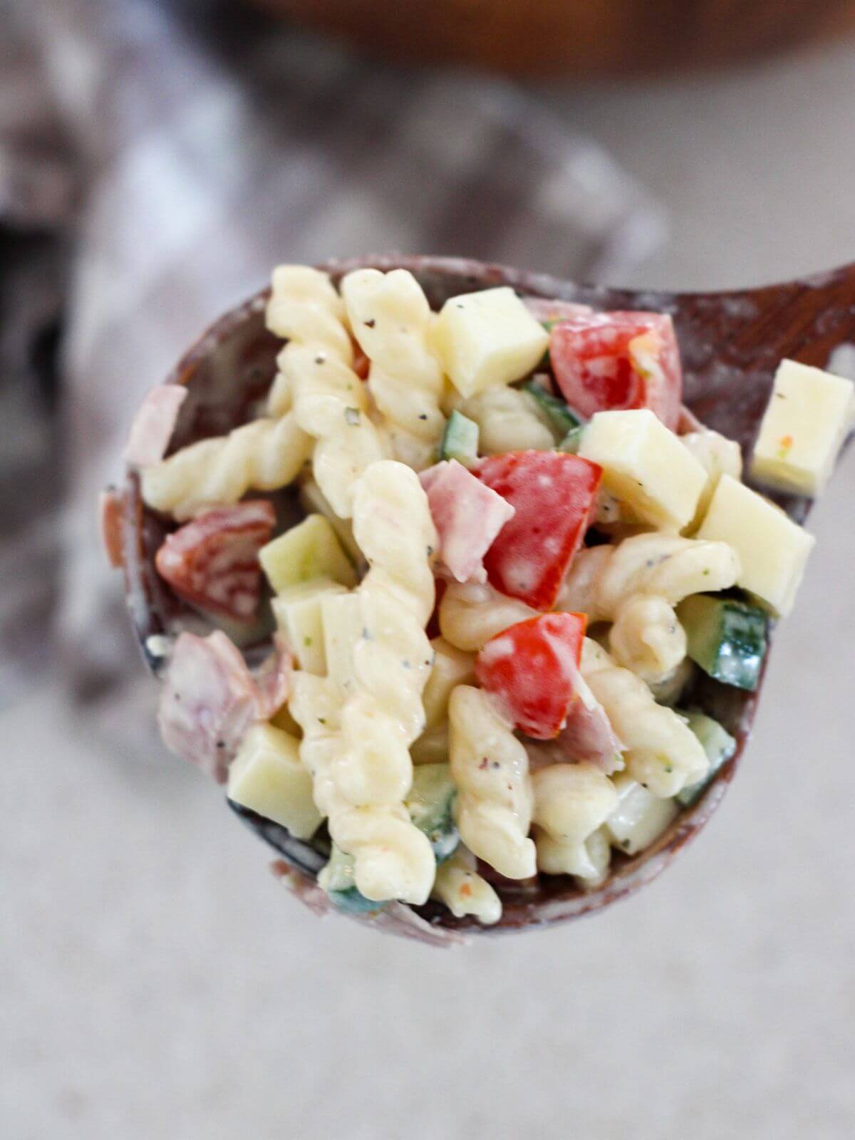 Pasta salad mixed all together and ready to eat on a wooden spoon