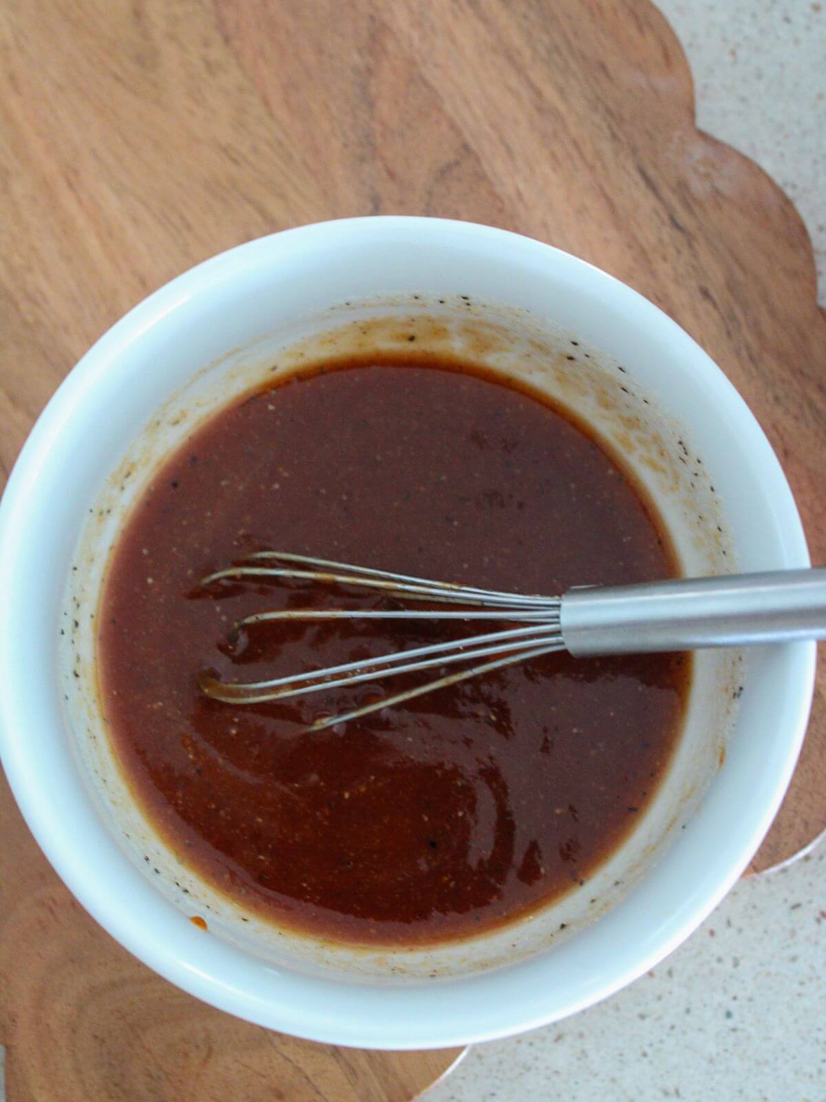 BBQ Sauce mixture in a white bowl with a silver whisk