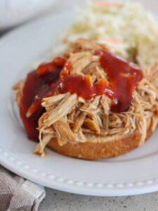 Crockpot Shredded BBQ Chicken Sandwich ready to eat on a bun with coleslaw in the background
