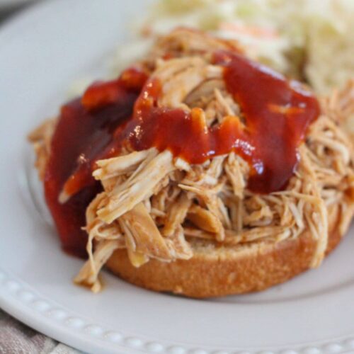 Crockpot Shredded BBQ Chicken Sandwich ready to eat on a bun with coleslaw in the background