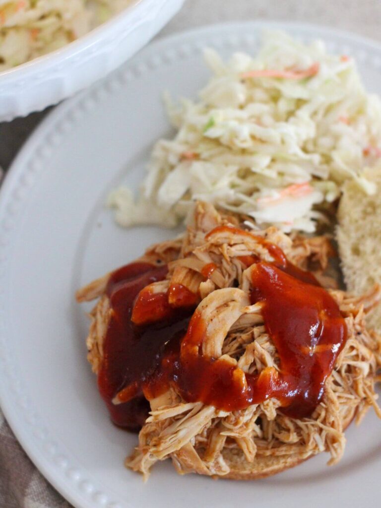 shredded bbq chicken on a bun with coleslaw on a white plate
