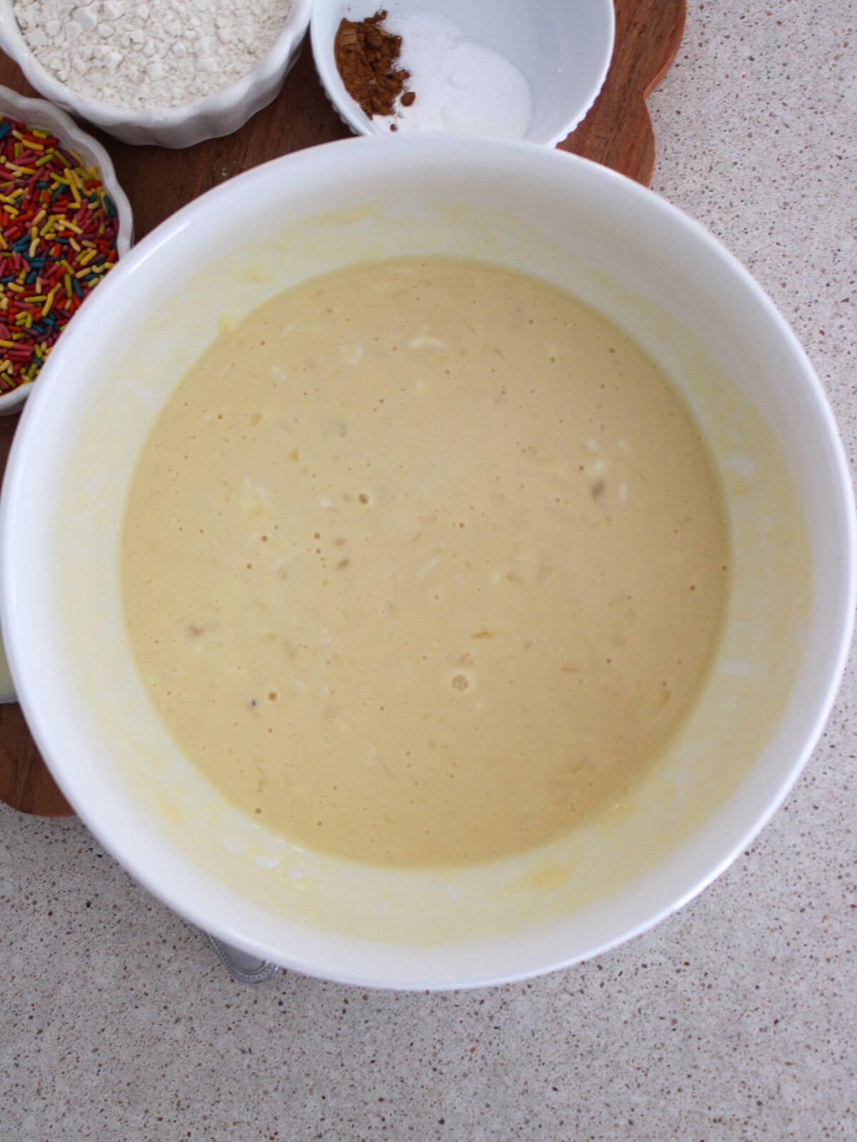 wet ingredients mixed into a white bowl with a cutting board with the rest of the ingredients behind it