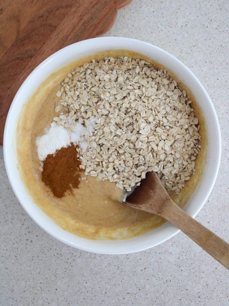 Adding the dry ingredients to the wet ingredient in the white bowl with a wooden spoon