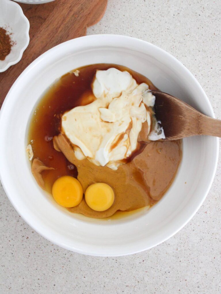 Mixing the wet ingredients in a white bowl with a wooden spoon