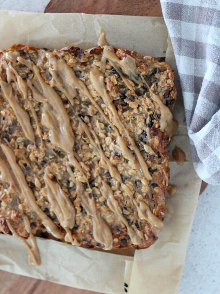 Peanut butter bars drizzled with peanut butter drizzle on parchment paper on a wooden cutting board with a plaid napkin
