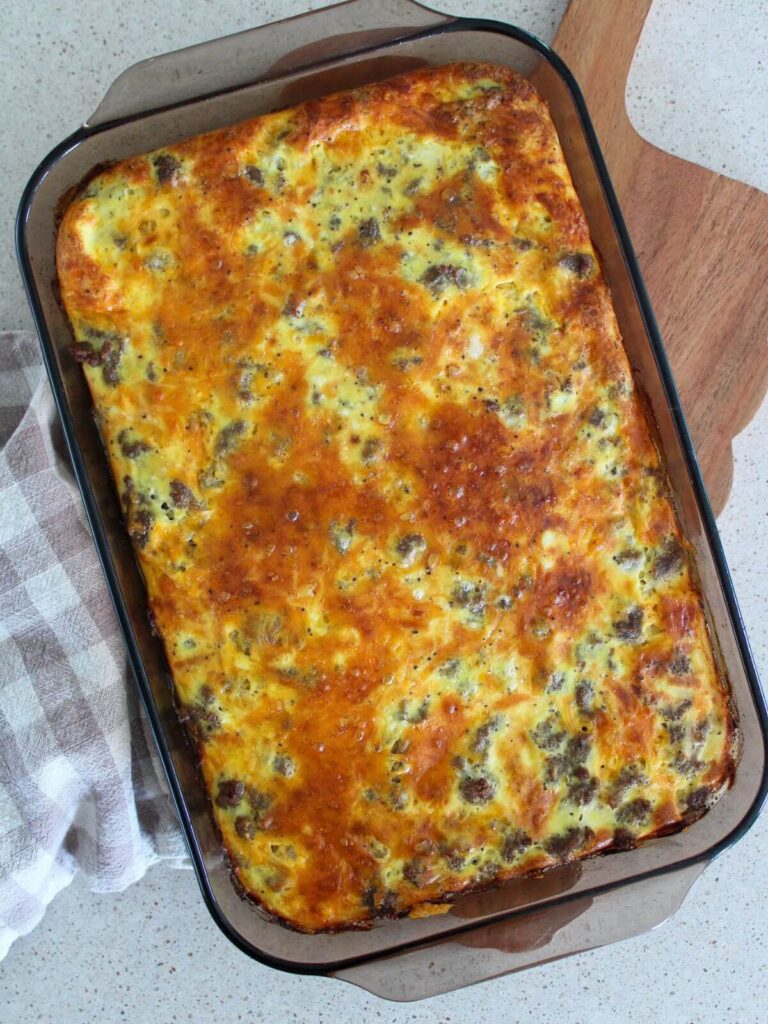 the turkey bacon sausage casserole cooked in the brown baking dish on a cutting board with a plaid towel