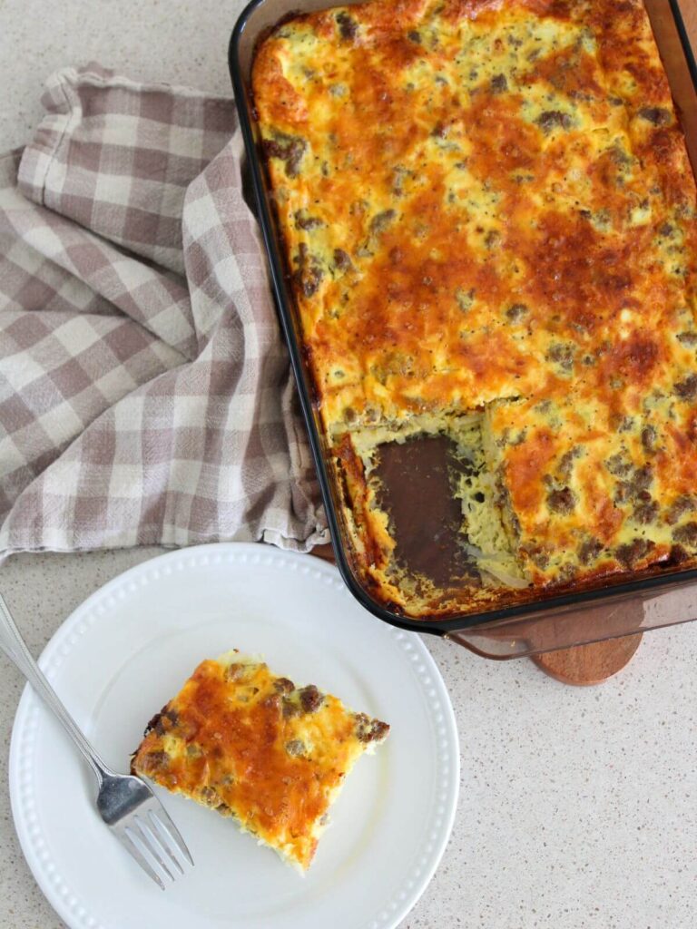 an overhead view of the casserole in the baking dish and a piece on a round white plate ready to eat with a fork and plaid napkin