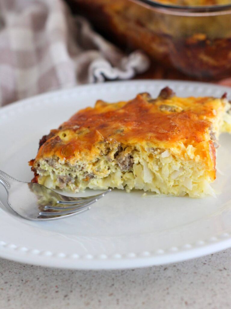 a piece of the casserole on a white plate with a silver fork with a plaid towel next to it