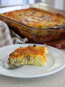 The finished casserole cut and placed on a white plate with a silver fork with the rest of the casserole in the background and a plaid towel