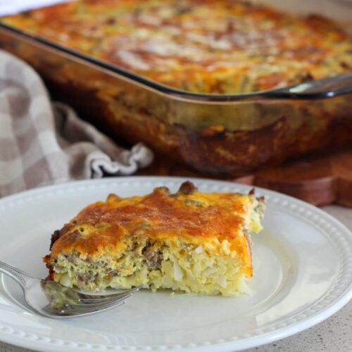The finished casserole cut and placed on a white plate with a silver fork with the rest of the casserole in the background and a plaid towel