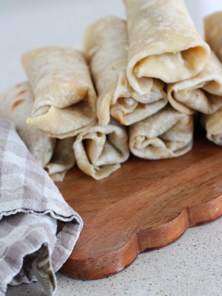 the burritos rolled and stacked on a brown cutting board with a plaid napkin