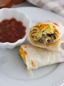 Easy Freezer Breakfast Burrito cut open on a white plate with a cup of salsa.