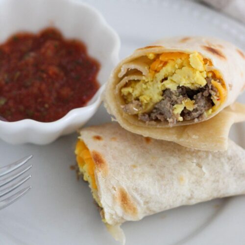 Easy Freezer Breakfast Burrito cut open on a white plate with a cup of salsa.
