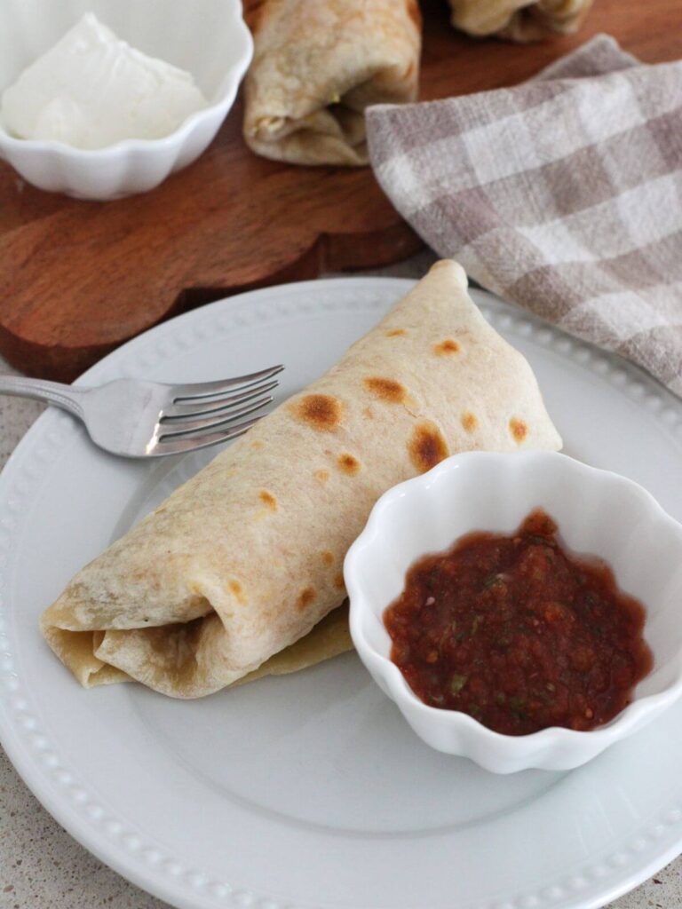 breakfast burrito on a plate with salsa in a bowl and a fork next to it. 