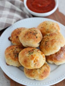 The Pizza bites stacked on a white plate with a plaid towel with a small white bowl of marinara