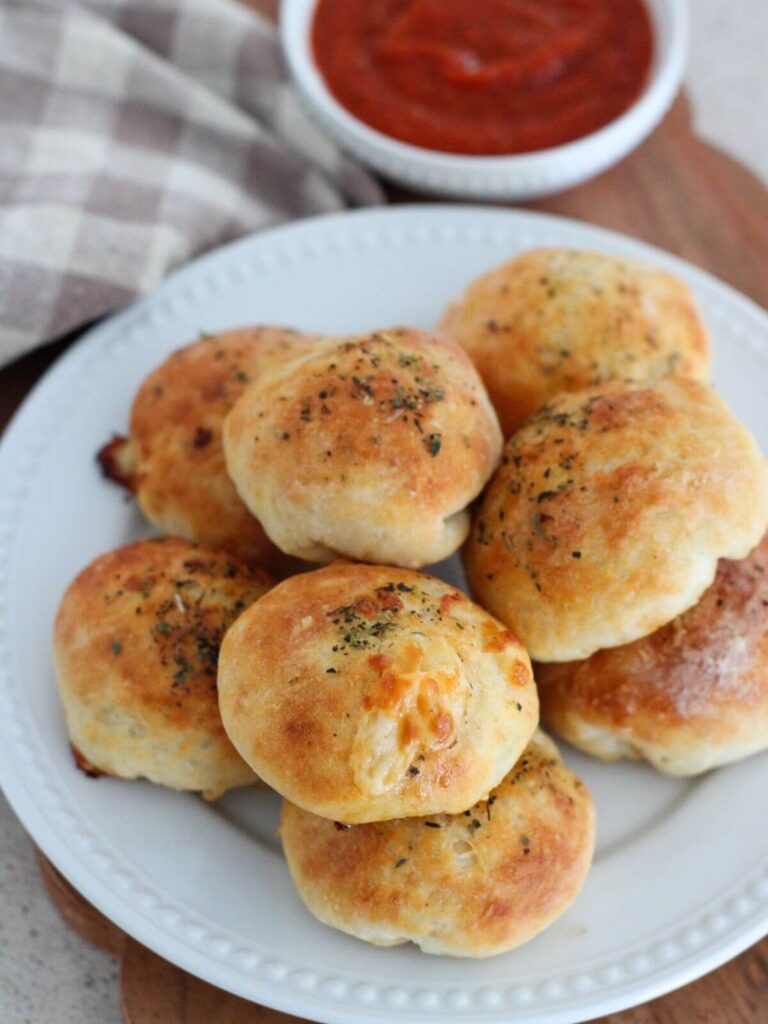 The Pizza bites stacked on a white plate with a plaid towel with a small white bowl of marinara