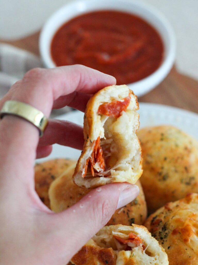 The pepperoni and cheese showing in the pizza bomb being held with others behind and marinara in a white bowl