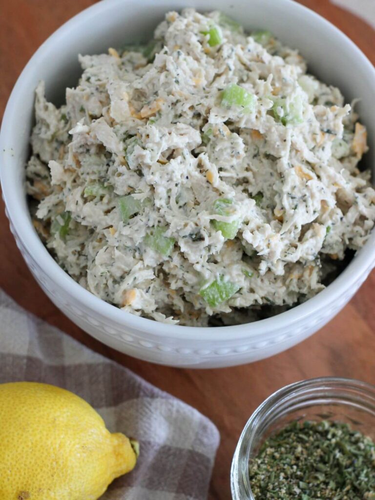 Ranch Chicken Salad in a white bowl on a cutting board with a lemon, ranch seasoning and a plaid towel around it