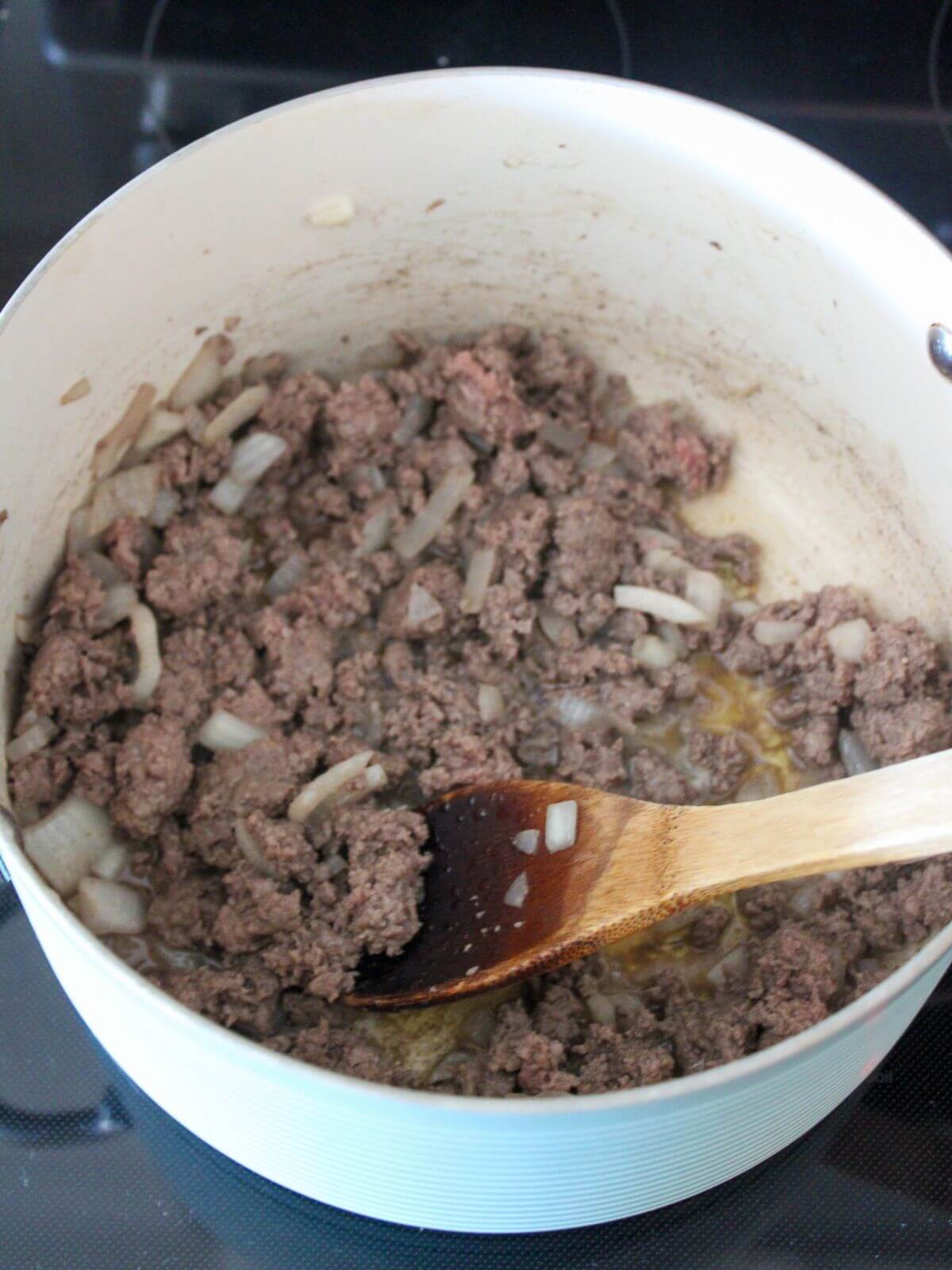 ground beef and onions cooking in butter in a blue stock pan