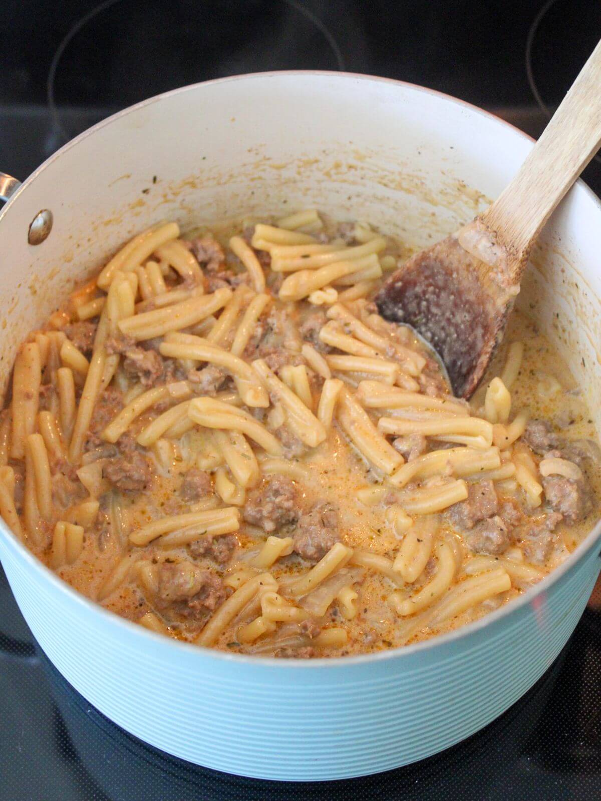cheeses and cream added to the mixture in the stock pan with a wooden spoon