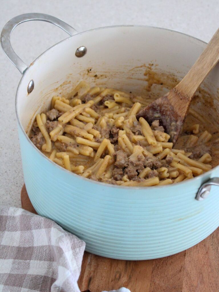 Ground Beef Pasta ready to eat in a blue stock pot with a wooden spoon on a wooden cutting board with a plaid napkin 