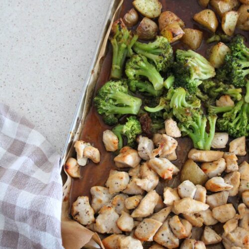 up close of the sheet pan honey garlic chicken on a sheet pan with parchment paper and a plaid napkin next to it