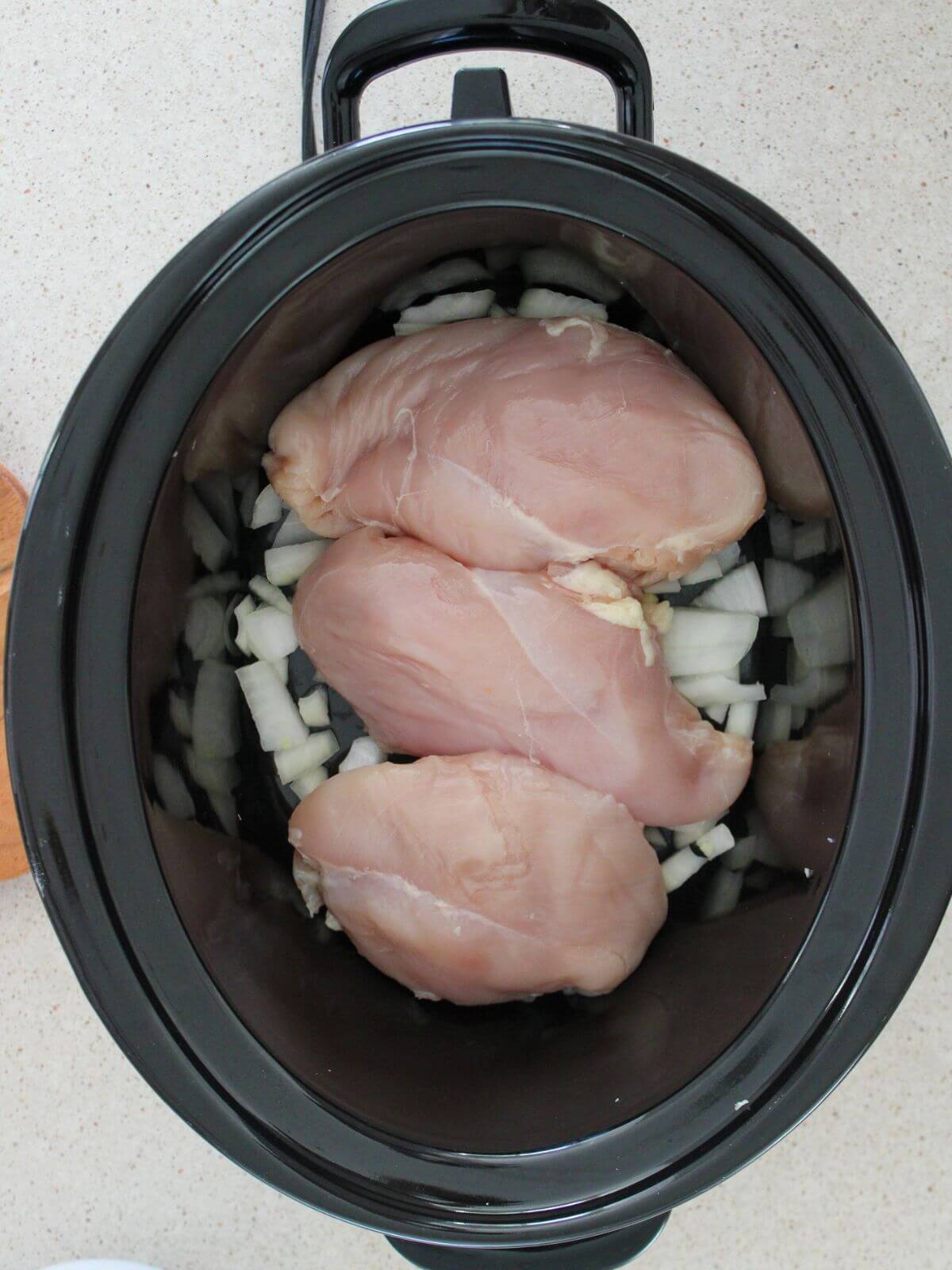 chicken on top of onions and garlic in a crockpot
