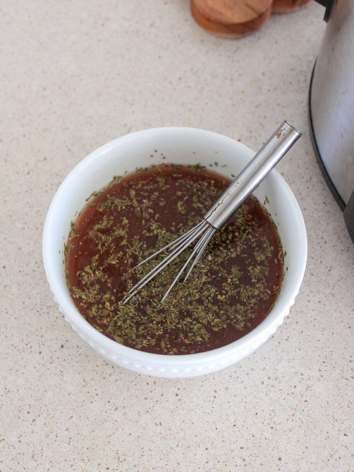 marinade ready to pour over the chicken in a white bowl with a silver whisk
