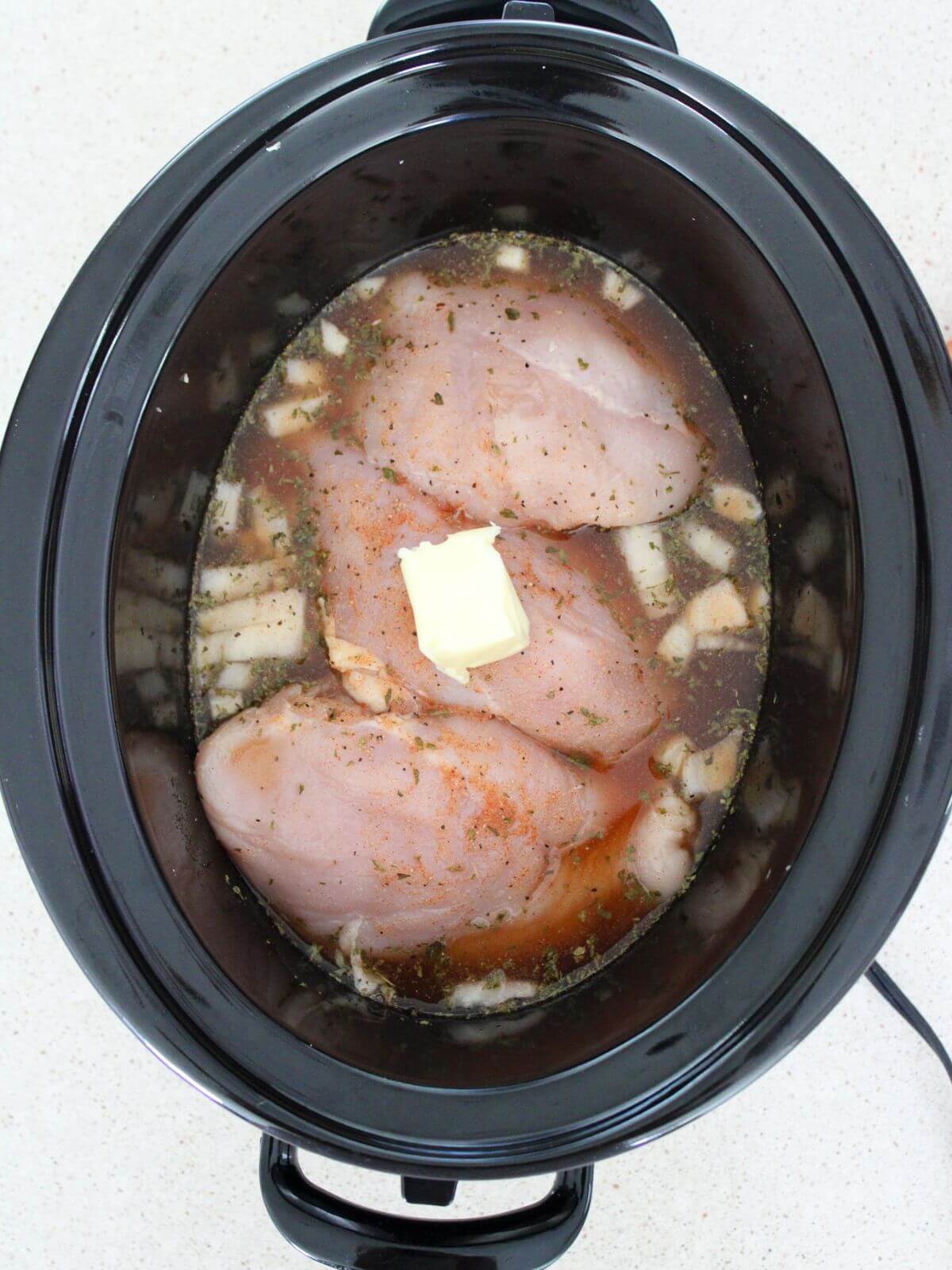 chicken, garlic, onions, and marinade topped with butter in a crockpot ready to cook