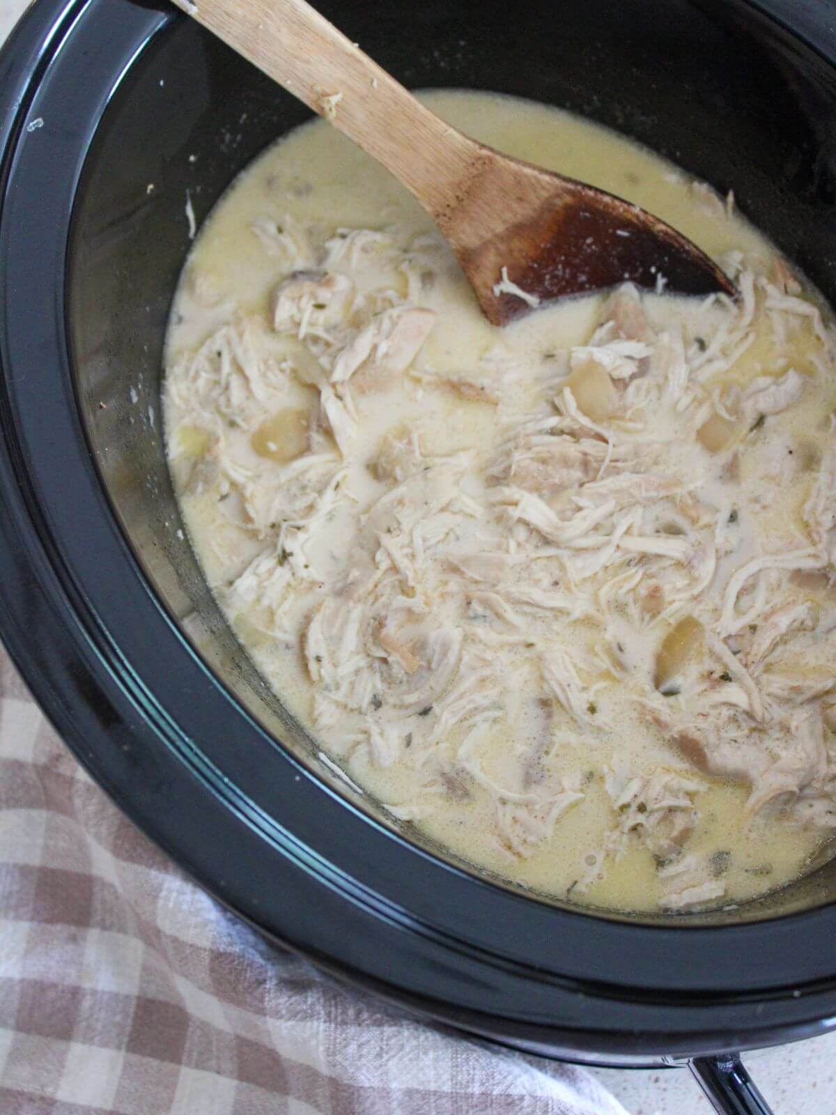 chicken and gravy ready to eat in a crockpot with a wooden spoon with a plaid napkin