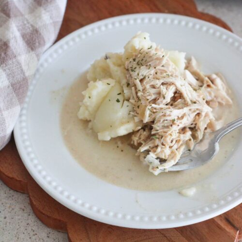 chicken and gravy over mashed potatoes on a white plate on a cutting board with a plaid napkin