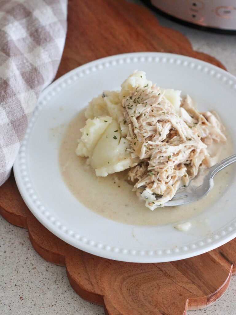 chicken and gravy over mashed potatoes on a white plate on a cutting board with a plaid napkin