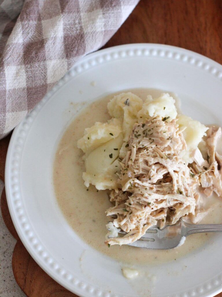 Slow Cooker Chicken and gravy on a white plate with a fork and a plaid napkin behind it