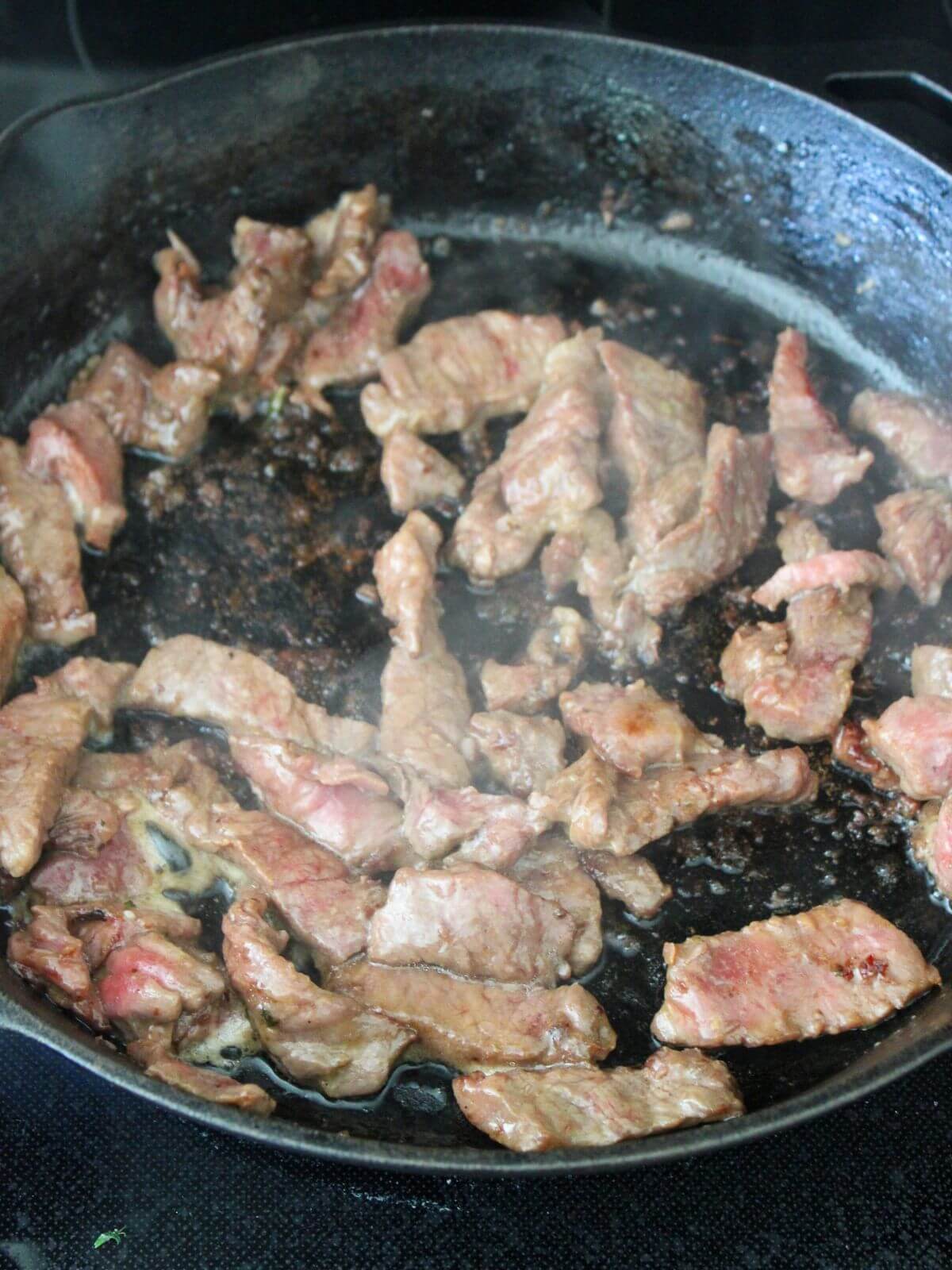 beef cooking in the cast-iron pan